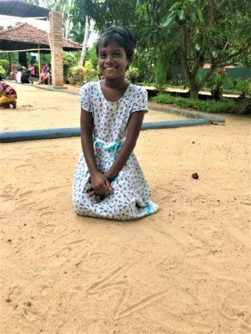 Maheshika schreibt ihren Namen in den Sand.