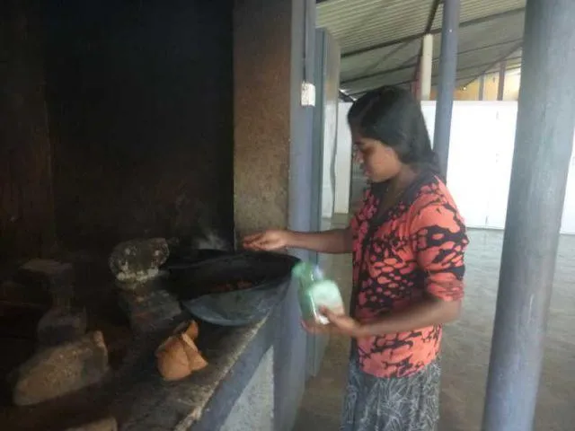 Nadeesha steht an der Feuerstelle und gibt Salz zum Curry.