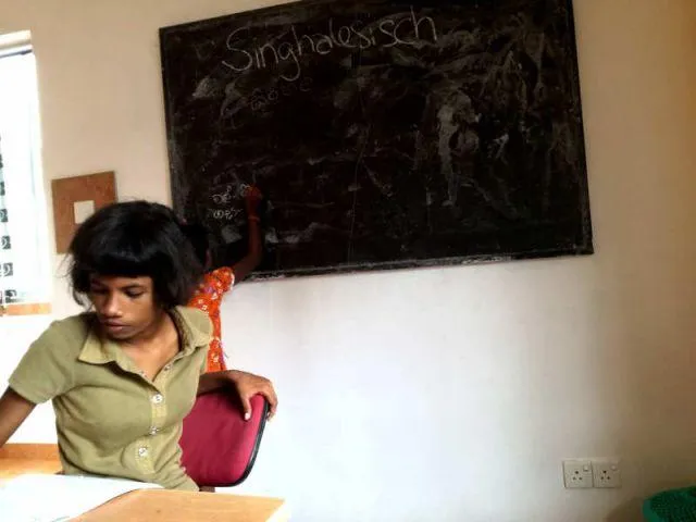 Man sieht Subani und Sachini im Klassenzimmer, w&auml;hrend sie versuchen singhalesische W&ouml;rter zu erkl&auml;ren.